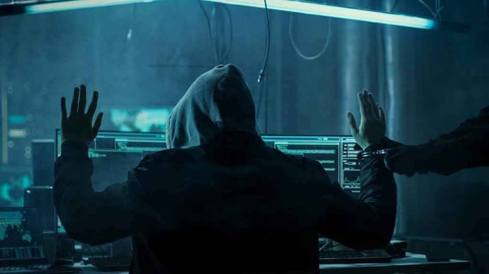 shutterstock_680075263 Hooded person at computer raises hands as another clamps handcuffs