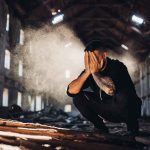 Man crouching in an abandoned warehouse with hands covering face