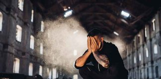 Man crouching in an abandoned warehouse with hands covering face