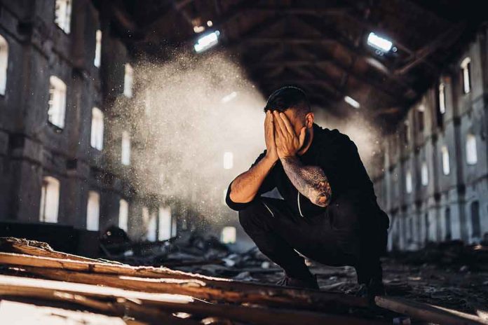 shutterstock_1018217620 Man crouching in an abandoned warehouse with hands covering face