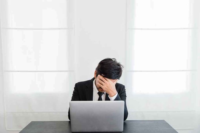 shutterstock_1020448816 man in suit covers face while sitting at laptop