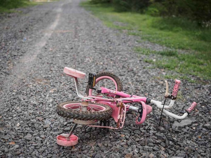shutterstock_1098020126 Pink children's bicycle with training wheels lying on a gravel path