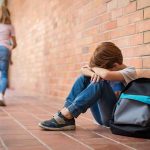 Mom Sent Her ‘Troubled’ Boy AWAY — Then Came His Test RESULTS boy sitting against brick wall with head on arms and backpack