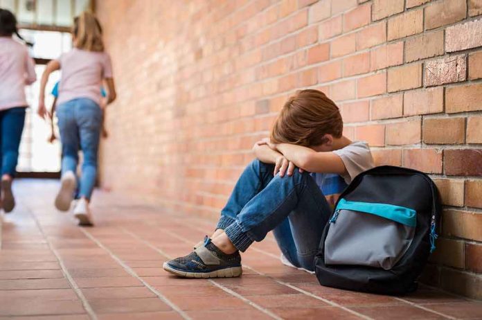 boy sitting against brick wall with head on arms and backpack
