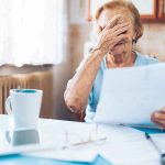 Social Security Raise Has A CATCH — What You Really KEEP Older woman covering her face while reading a document at a kitchen table
