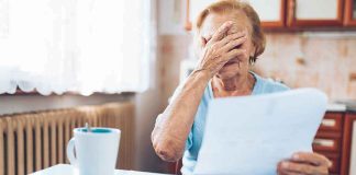 Older woman covering her face while reading a document at a kitchen table