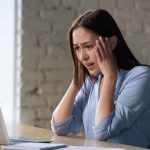 Concerned woman looking at laptop with hands on her head