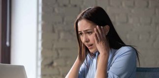 Concerned woman looking at laptop with hands on her head
