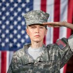 soldier in camouflage uniform saluting in front of a U.S. flag