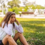 Young woman sitting on grass holding her head