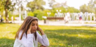Young woman sitting on grass holding her head