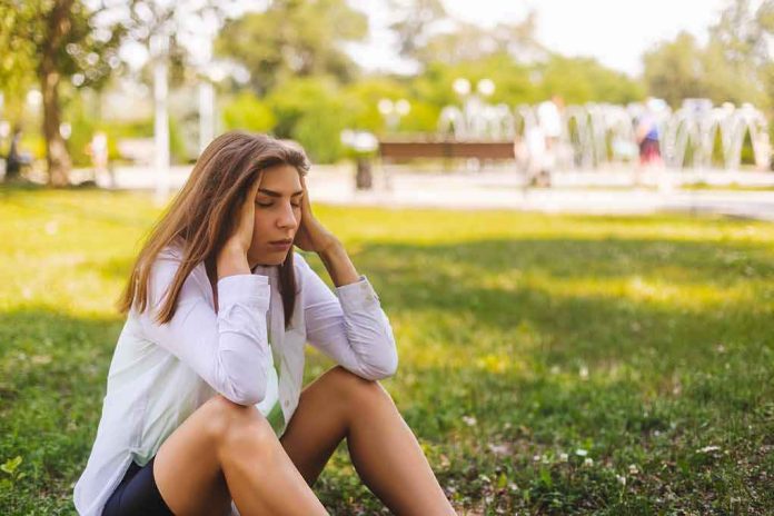 Young woman sitting on grass holding her head