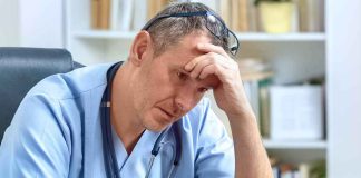 doctor in scrubs sitting with hand on forehead
