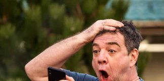 Exasperated man pressing a hand to his forehead while reading his phone