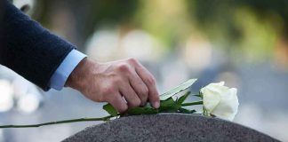hand placing white rose on gravestone