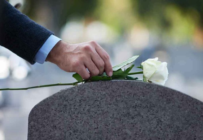 shutterstock_2129308964 hand placing white rose on gravestone