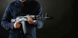 Would-Be Mass Killer’s Weapon Hid A BRILLIANT Secret person holding a rifle against a dark background