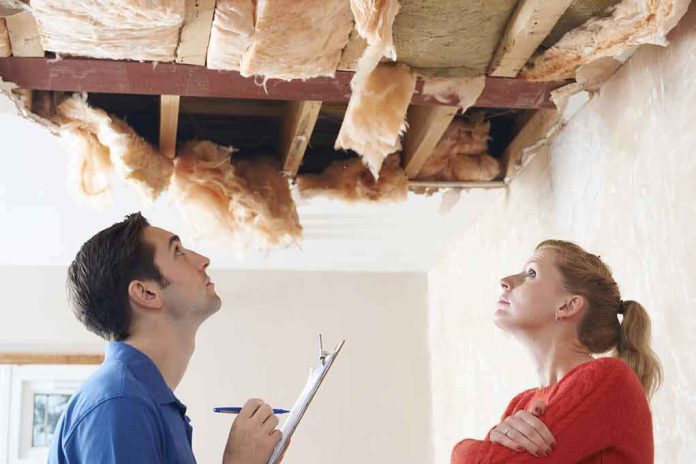 Two people inspecting a damaged ceiling with exposed insulation