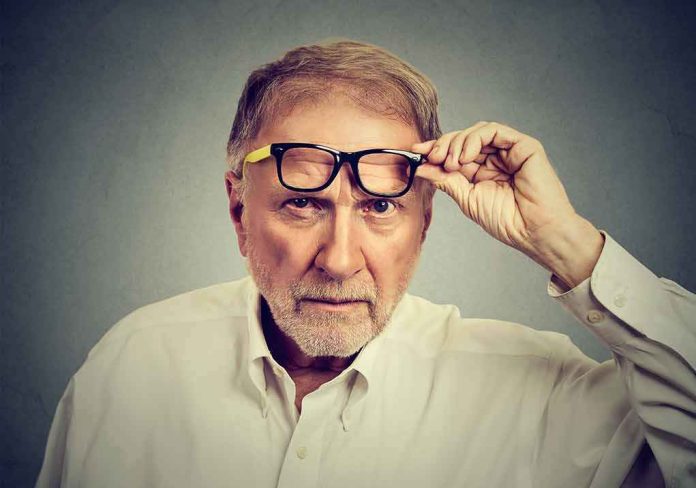 shutterstock_611173826 Older man lifting eyeglasses while looking intently at camera