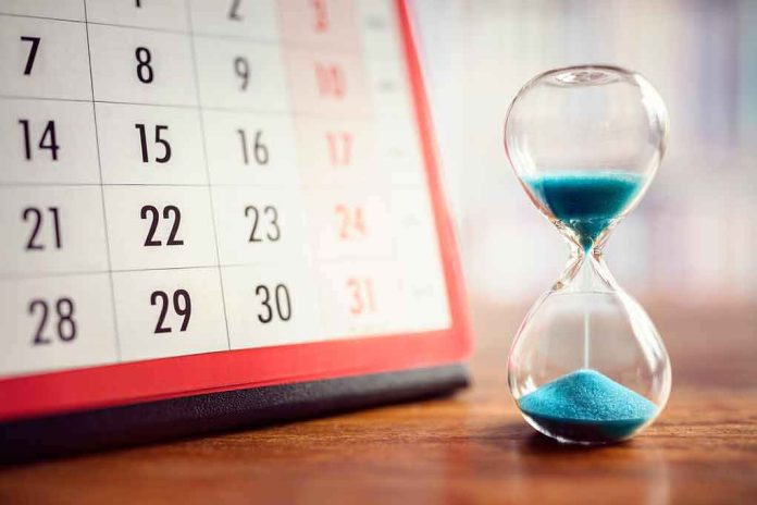shutterstock_767539465 Hourglass with blue sand beside a desk calendar